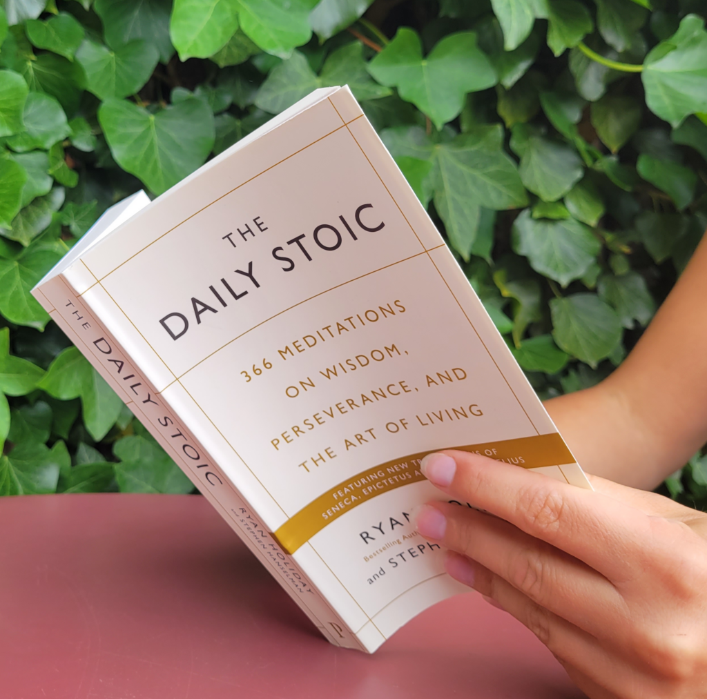 A woman reading The Daily Stoic: 366 Meditations on Wisdom, Perseverance, and the Art of Living by Ryan Holiday and Stephen Hanselman outside