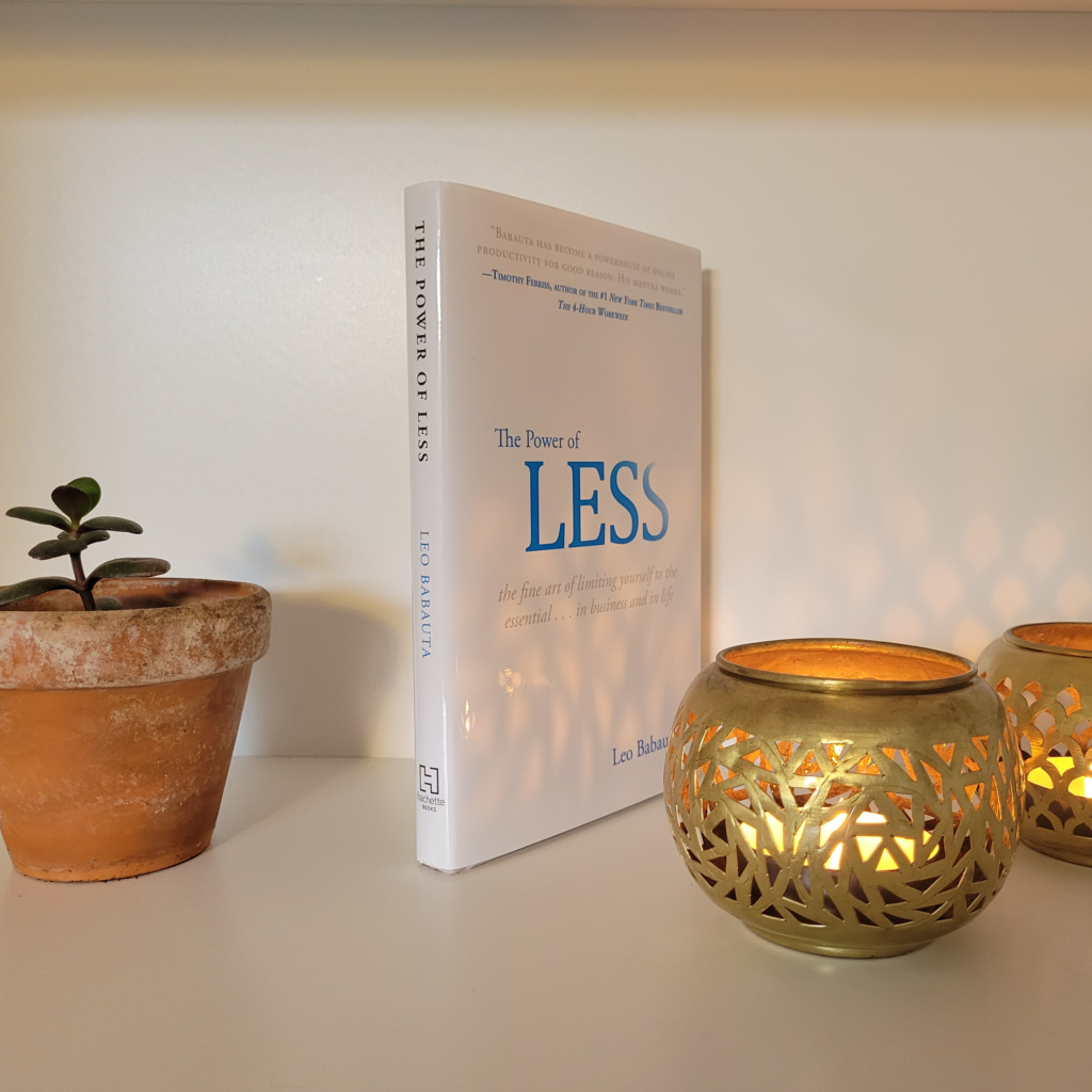 The Power of Less: The Fine Art of Limiting Yourself to the Essential by Leo Babauta on a bookshelf next to two candles and a plant